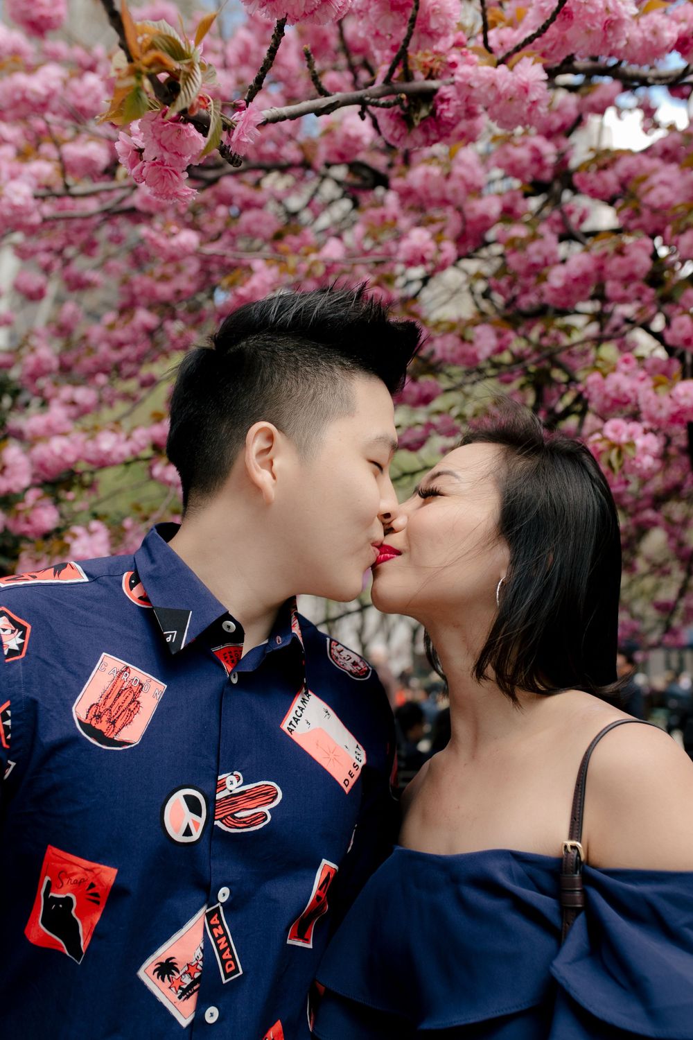 Couple sharing a romantic kiss under blooming pink cherry blossom trees in spring.