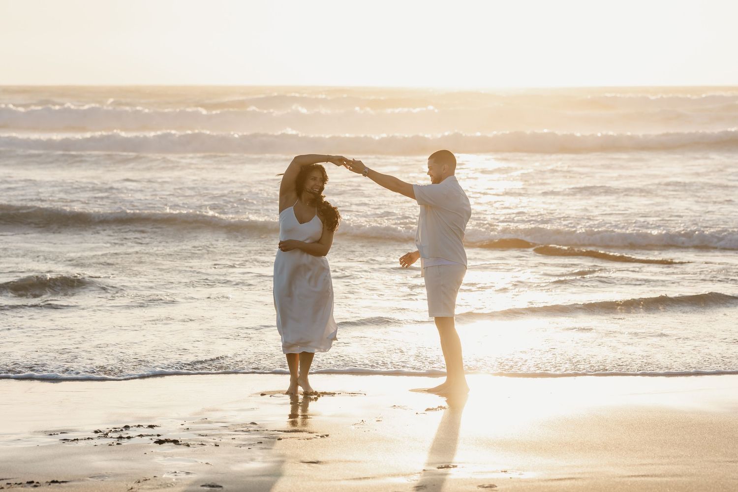 Couple dancing romantically on a sandy beach at golden sunset with ocean waves in the background.