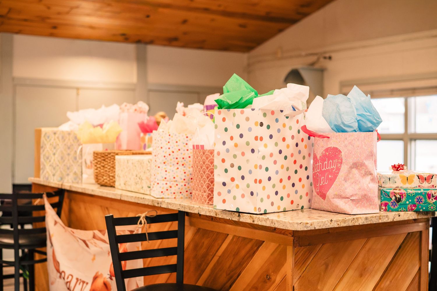 Colorful gift bags with tissue paper displayed on a wooden counter at a party or baby shower celebration.