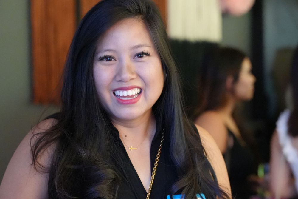 Smiling young woman with long dark hair at an indoor social gathering event.