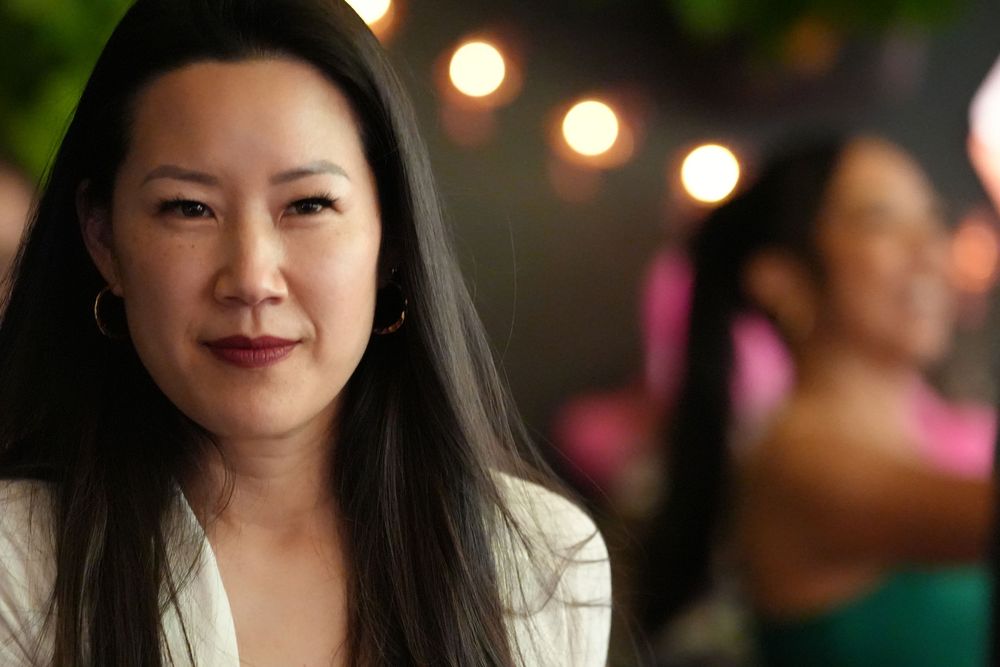 Elegant woman with long dark hair posing confidently at a bokeh-lit evening event.