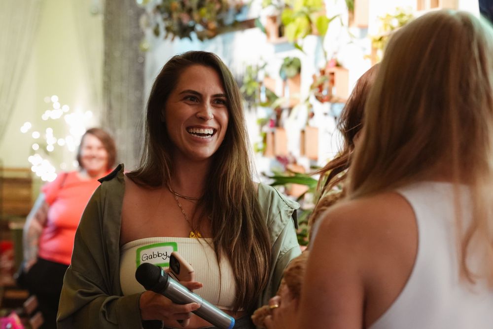 Woman smiling and holding a Ben & Jerry's ice cream cup at a vibrant indoor floral event.