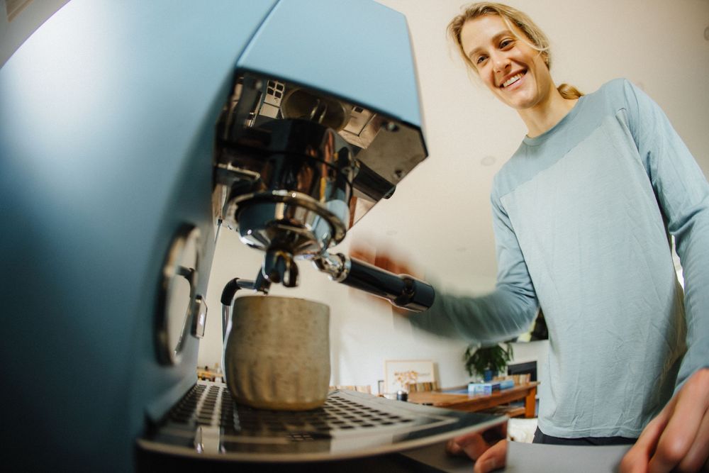 Smiling woman using a professional espresso machine to brew fresh coffee in a bright kitchen.