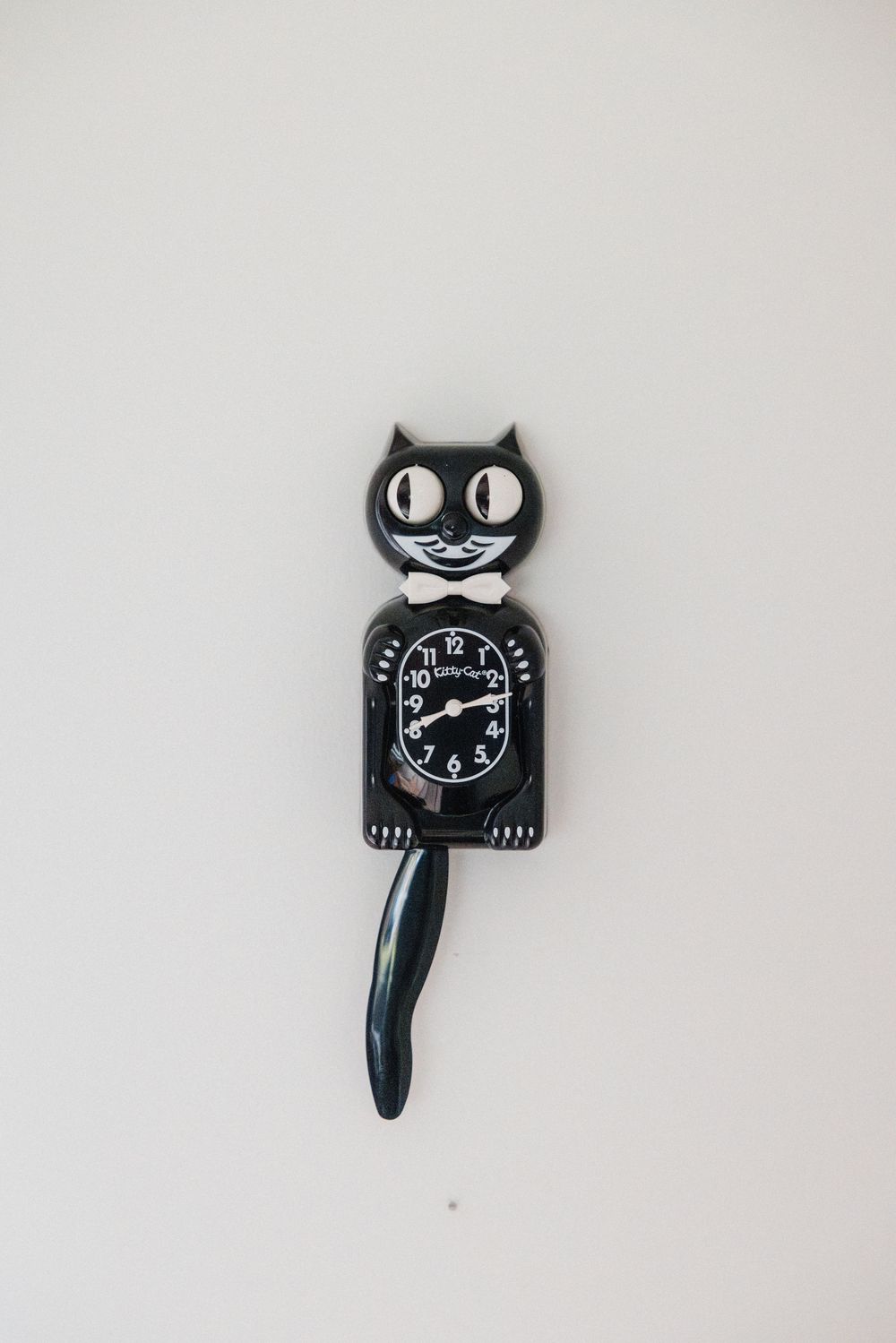 Black Kit-Cat Klock wall clock with moving tail and eyes, mounted on a white wall.