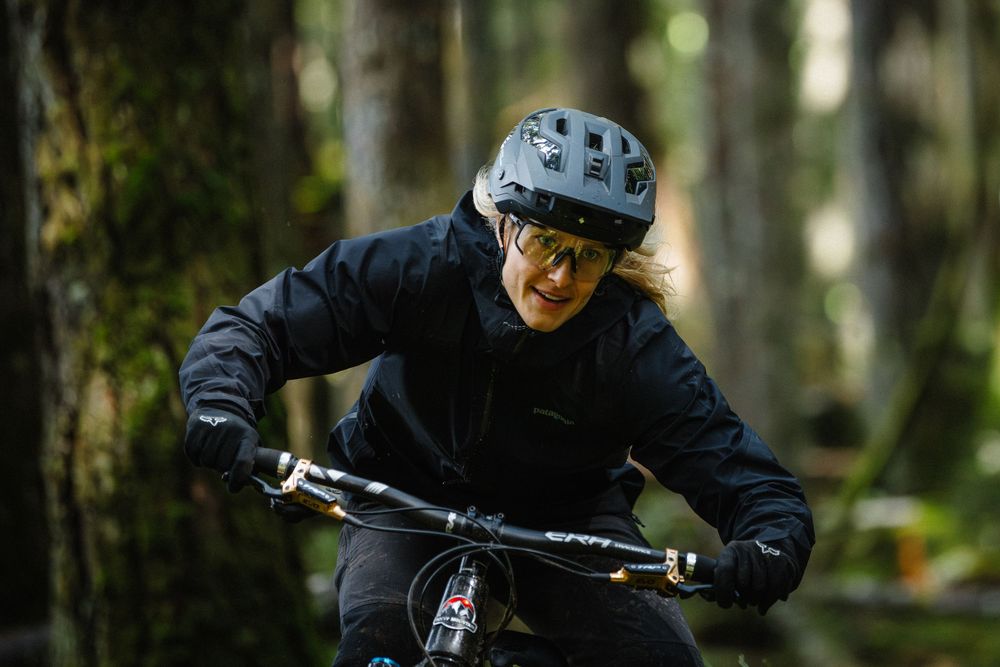 Woman mountain biker in black jacket and helmet rides through forest trail.