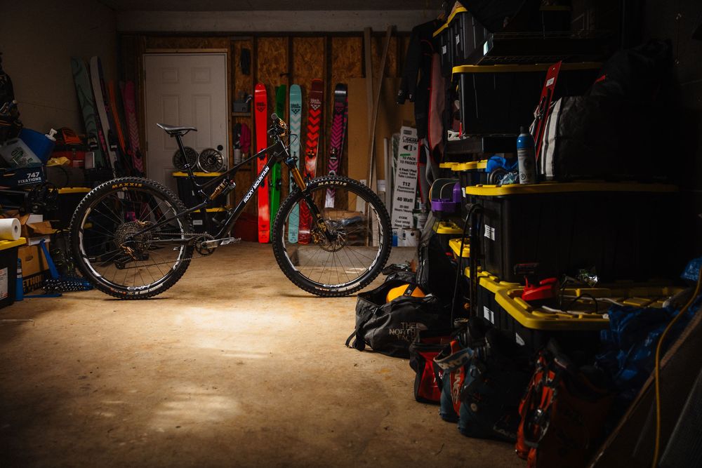 Mountain bikes stored in dimly lit garage with shelving units and sports equipment.