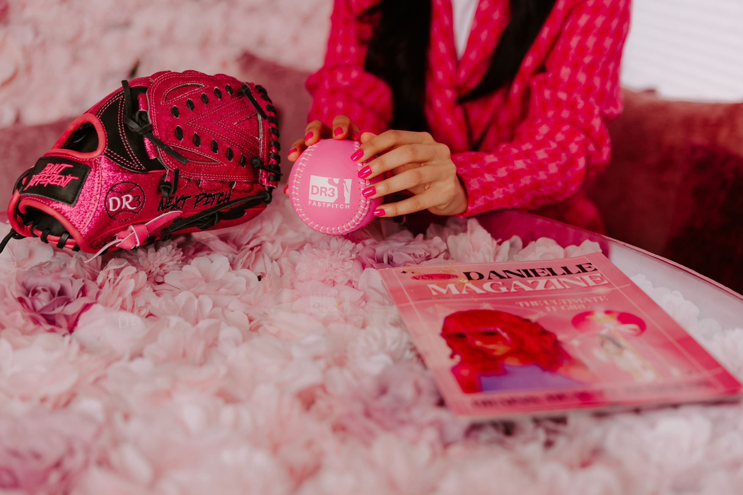 Pink baseball glove, Danielle Magazine, and pink accessories arranged on a fluffy pink surface.