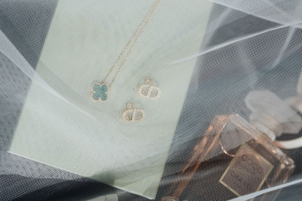 Gold clover necklace and stud earrings on green card beside perfume bottle.