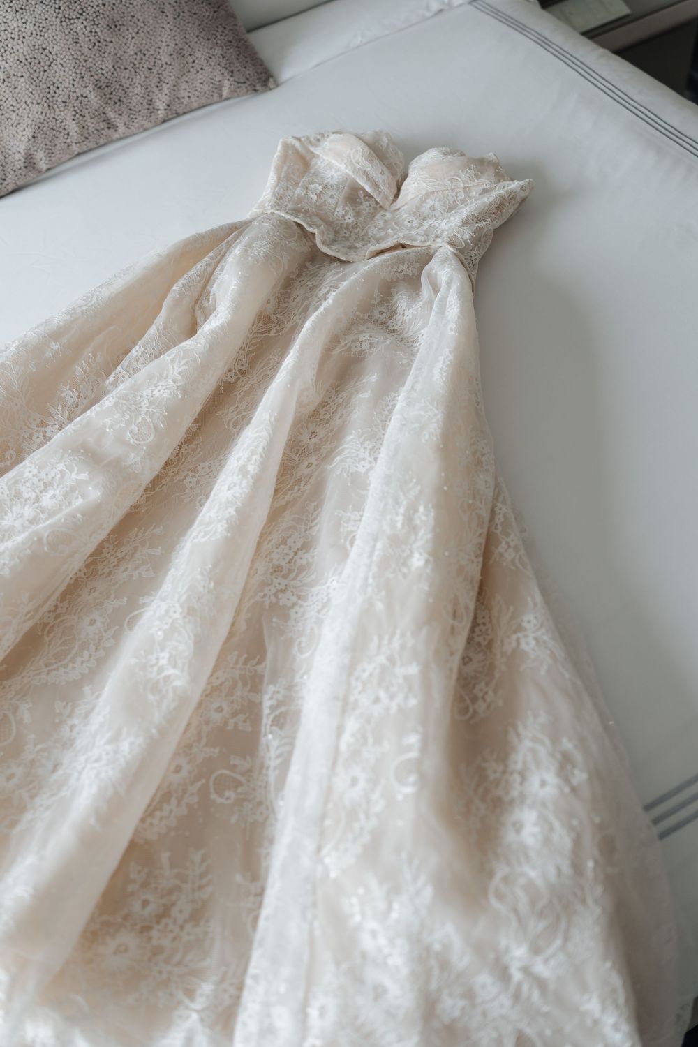Elegant strapless lace wedding dress in blush ivory displayed on a white surface with intricate floral lace detailing.
