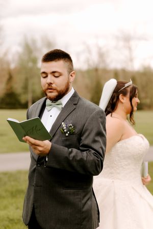 Groom in gray suit and bow tie reads letter back-to-back with bride in strapless white wedding gown.