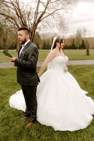 Bride and groom exchange private vows back-to-back on green lawn, each reading from small booklets.