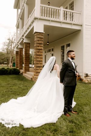 Bride and groom stand back-to-back on lawn in front of elegant white venue with stone columns.