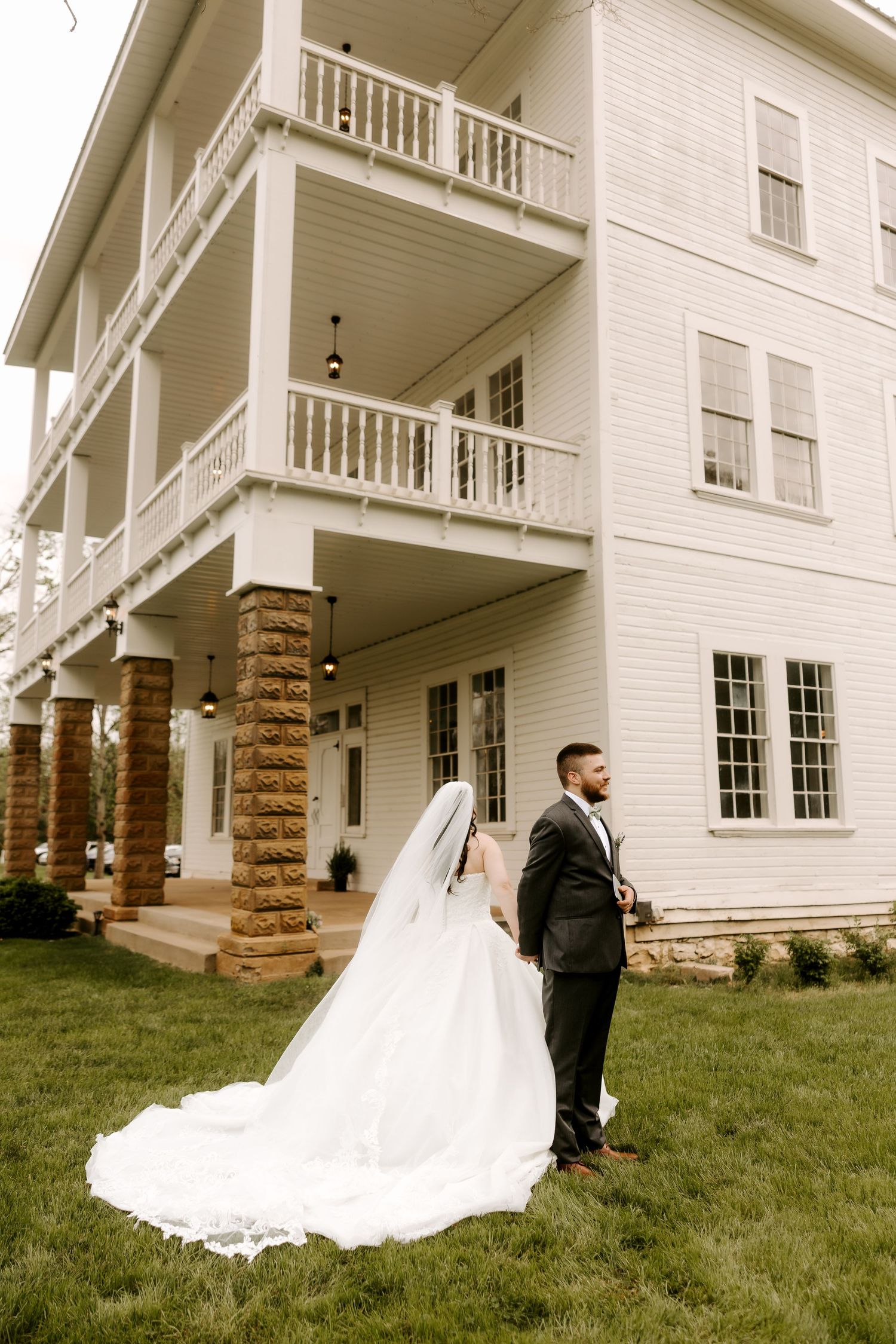 Bride and groom hold hands facing historic white multi-story venue with stone columns and balconies.
