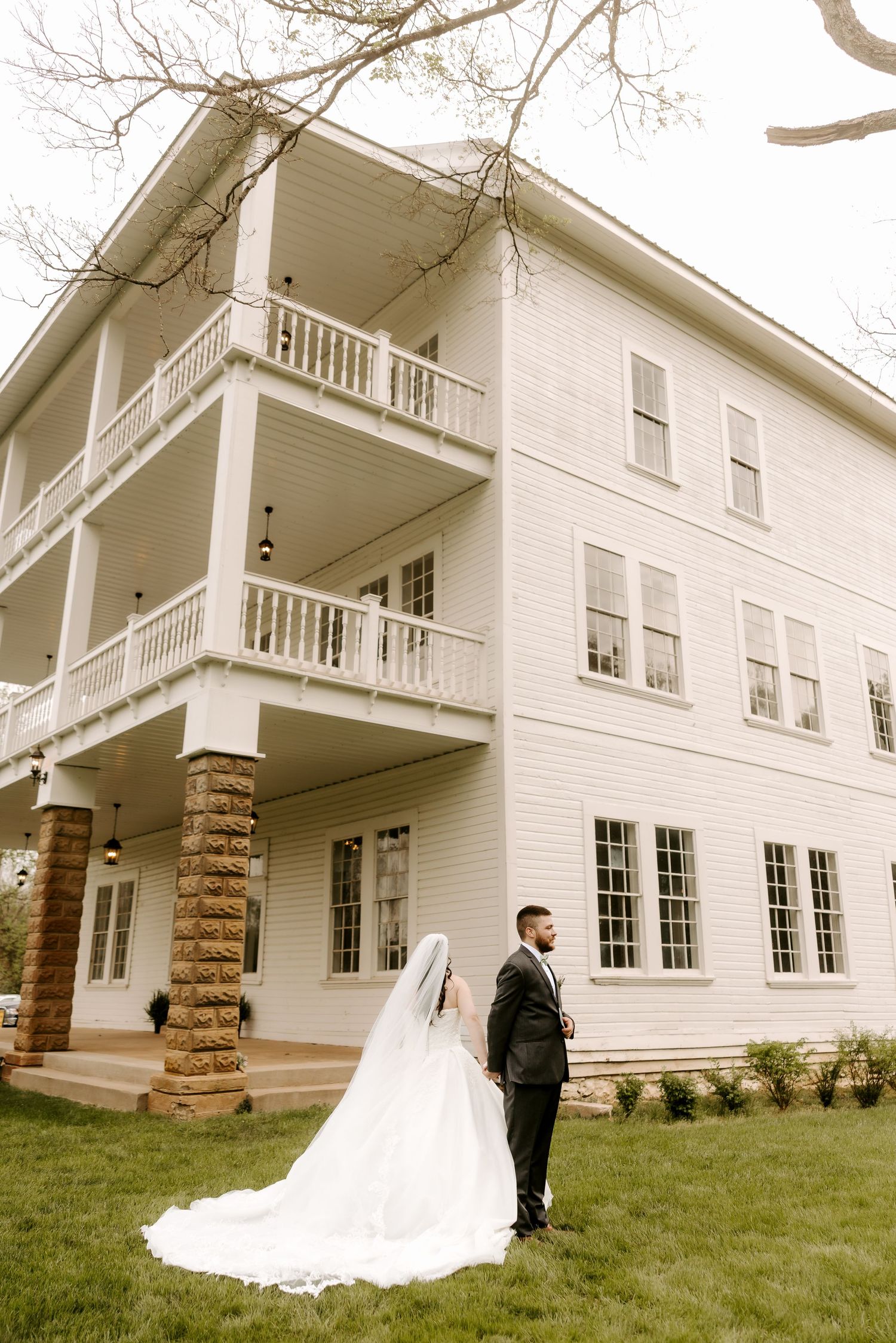 Bride and groom posing in front of elegant white three-story wedding venue with stone columns.