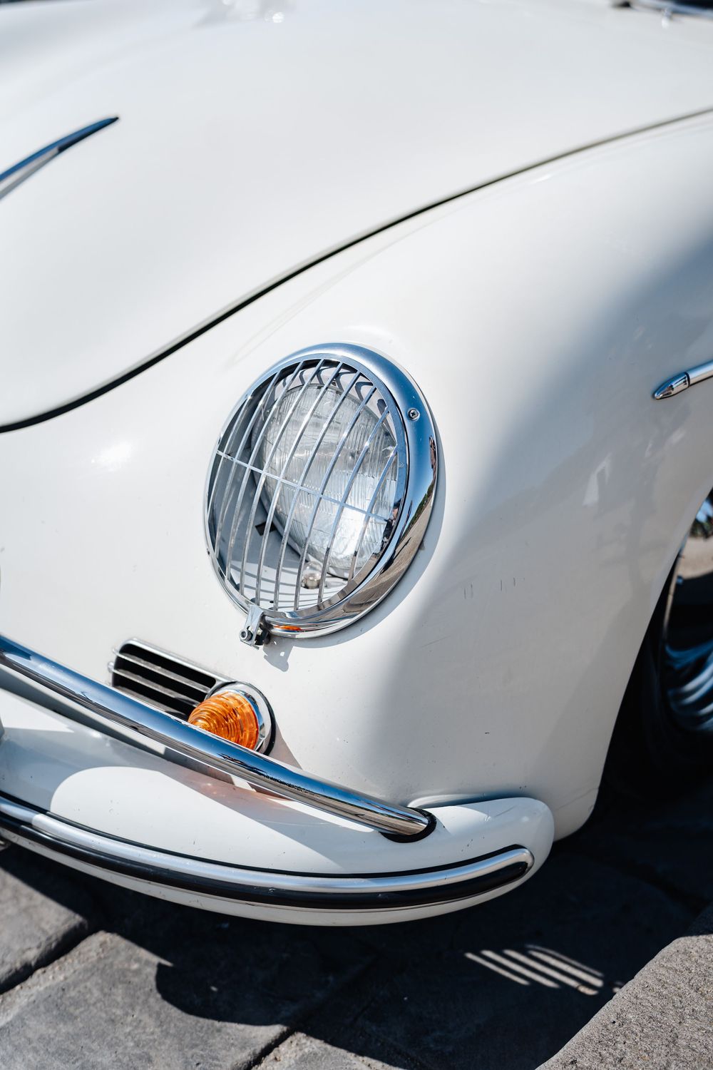Close-up of a classic white vintage car headlight with chrome grille guard and amber turn signal.