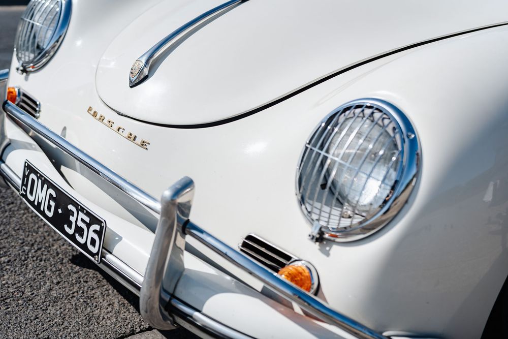 Close-up of a classic white Porsche 356 vintage car with chrome headlights and OMG-356 license plate.