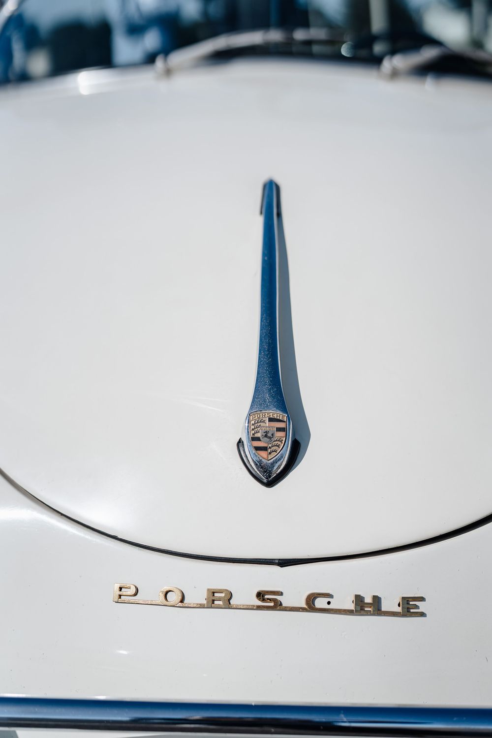 Close-up of a vintage white Porsche hood ornament and chrome lettering badge on a classic car.
