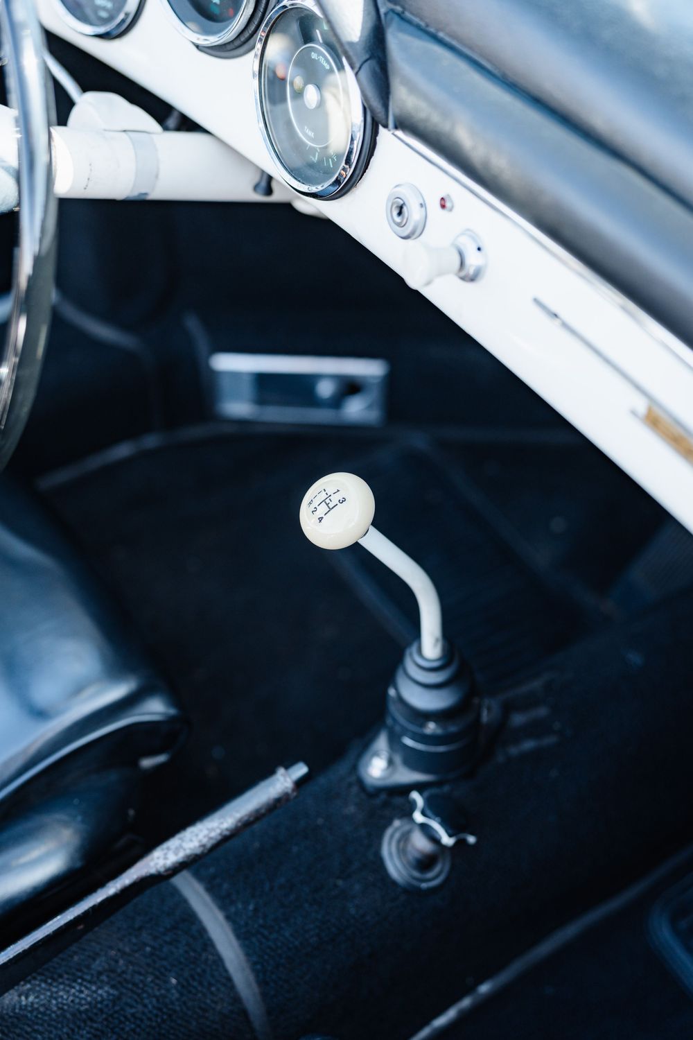 Vintage car interior featuring a white manual gear shift knob, dashboard gauges, and classic black upholstery.