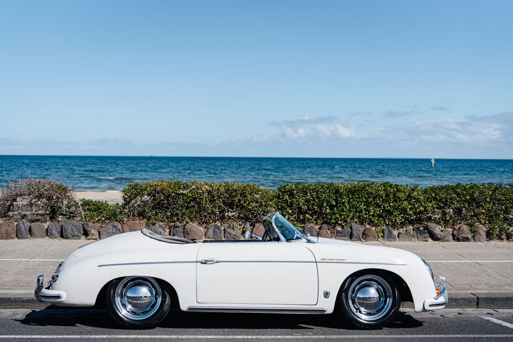White vintage Porsche 356 Speedster convertible parked by the ocean on a sunny day.