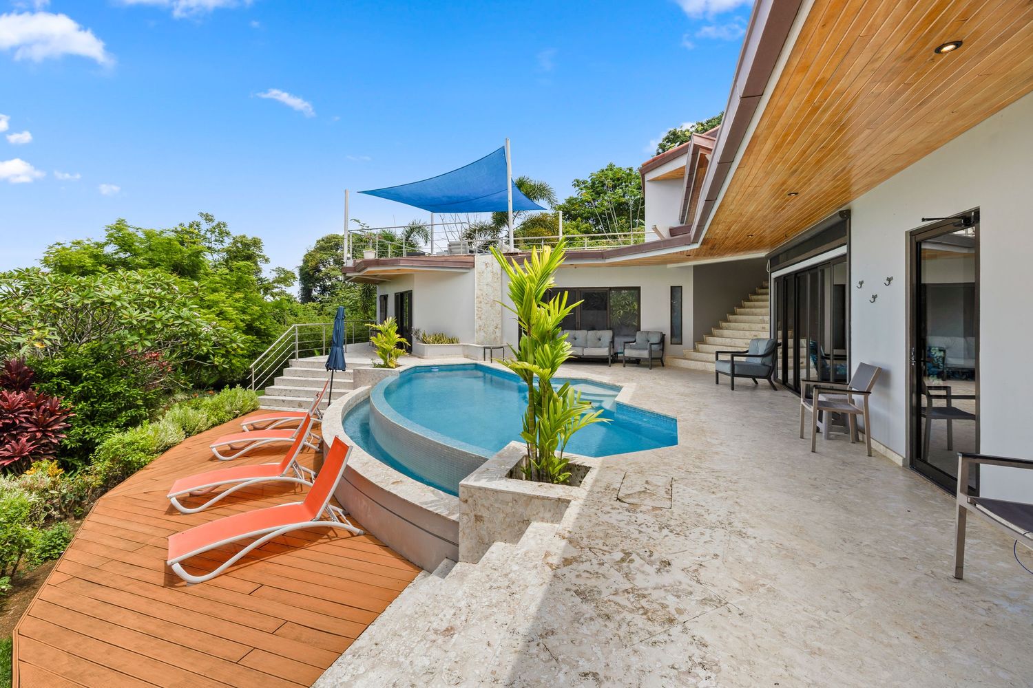 Luxury villa with curved mosaic-tiled pool, outdoor lounge seating, modern architecture, and lush tropical surroundings.