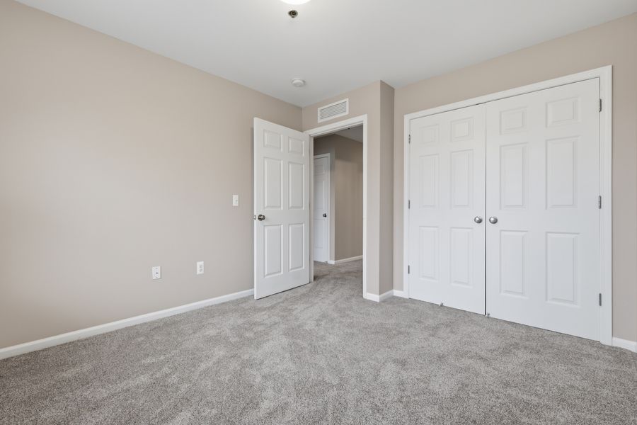 Spacious bedroom with gray carpet, white closet doors, and neutral beige walls in a modern apartment.