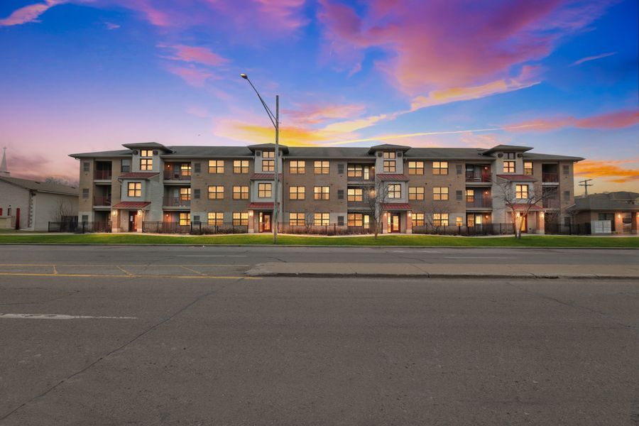 Modern 3-story apartment complex glowing at sunset with vibrant pink and blue sky backdrop along a quiet street.