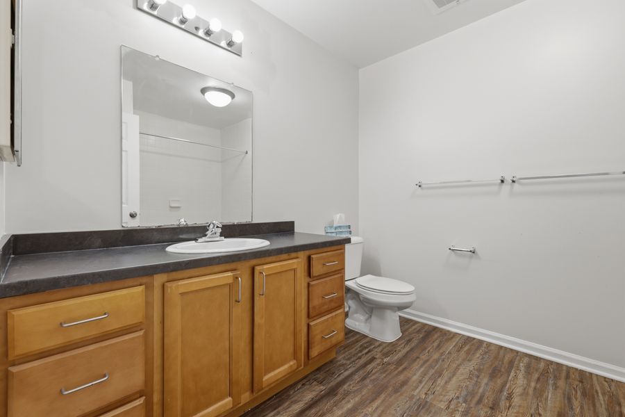 Bathroom with wooden vanity, dark countertop, large mirror, toilet, and hardwood floors in a clean, well-lit space.