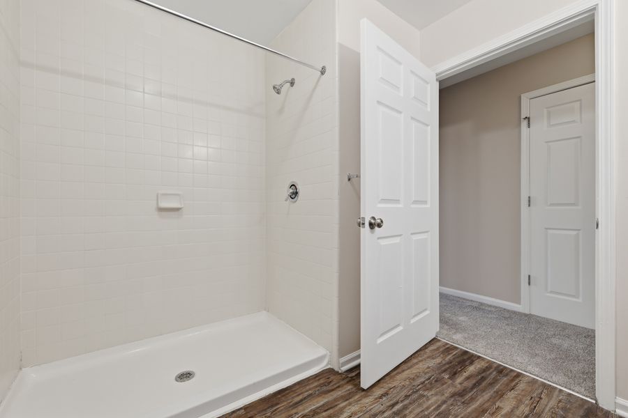 Modern bathroom with white subway tile walk-in shower, dark hardwood floors, and open door to carpeted room.