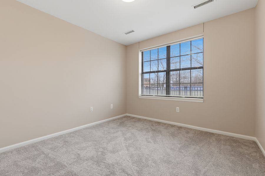 Empty bedroom with beige carpet, neutral walls, and a large window providing natural light.
