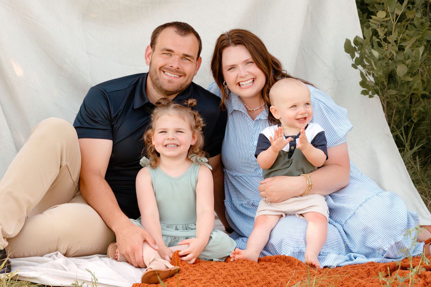 Warm outdoor family session with young kids, playful connection, green tones, soft backdrop and soft filmy texture.