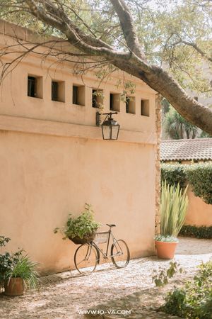 Rustic Mediterranean courtyard with a bicycle, terracotta walls, lantern, and lush potted plants.
