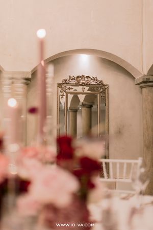 Elegant wedding reception with pink candles, red roses, and a ornate gold mirror in a classic arched venue.