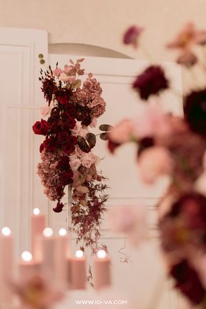 Elegant wedding floral arrangement with deep red and blush pink roses, cascading blooms, and glowing candles in soft light.