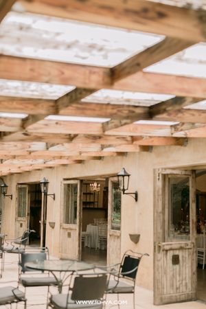 Rustic outdoor patio with wooden pergola, vintage doors, and elegant table settings at a wedding venue.