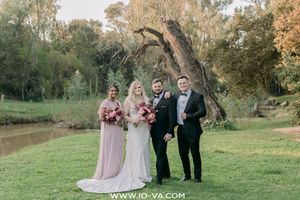 Wedding party of four posing outdoors near a river, featuring bride in white gown and bridesmaid in pink dress.