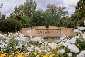 Avianto venue entrance sign surrounded by lush greenery and colorful white and yellow roses in full bloom.