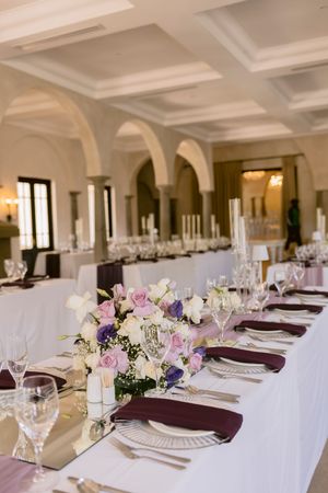 Elegant wedding reception hall with long tables set with burgundy napkins, crystal glasses, and pink and white floral centerpieces.