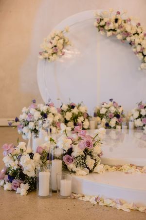 Elegant wedding altar with white and purple floral arrangements, candles, and a circular arch backdrop.