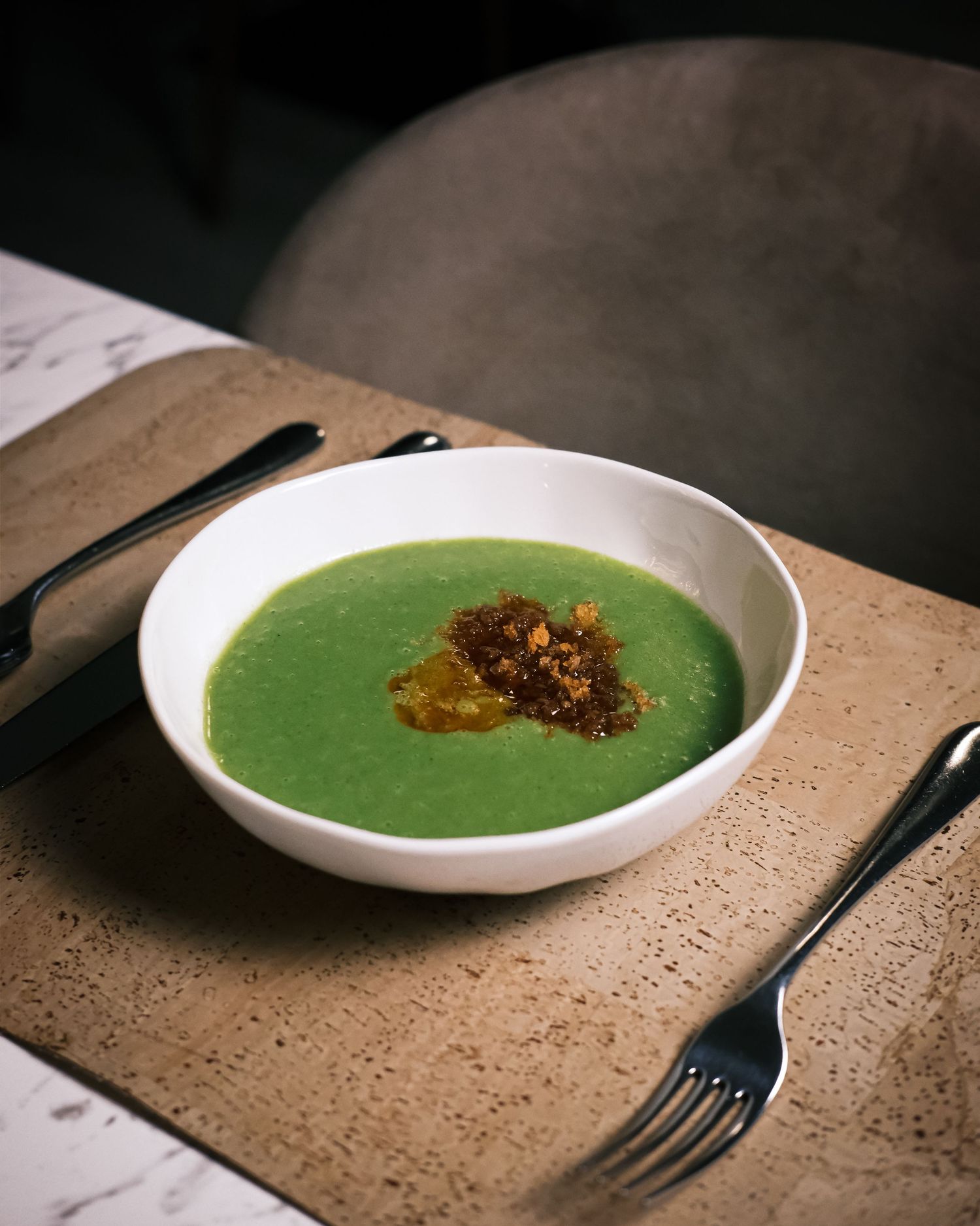Vibrant green pea soup topped with crispy golden garnish served in white bowl on wooden board.