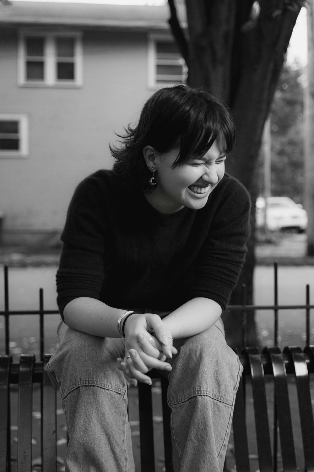 Black and white high school senior of someone in dark sweater sitting on railing, showing genuine laughter.