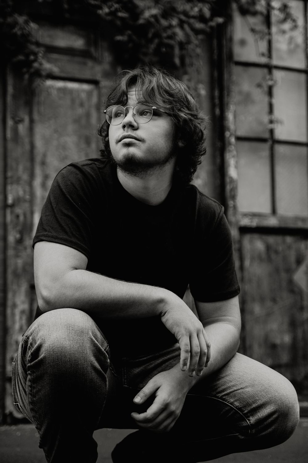 Dramatic black and white high school senior portrait of someone in glasses and t-shirt against textured wall. Dayton, Ohio