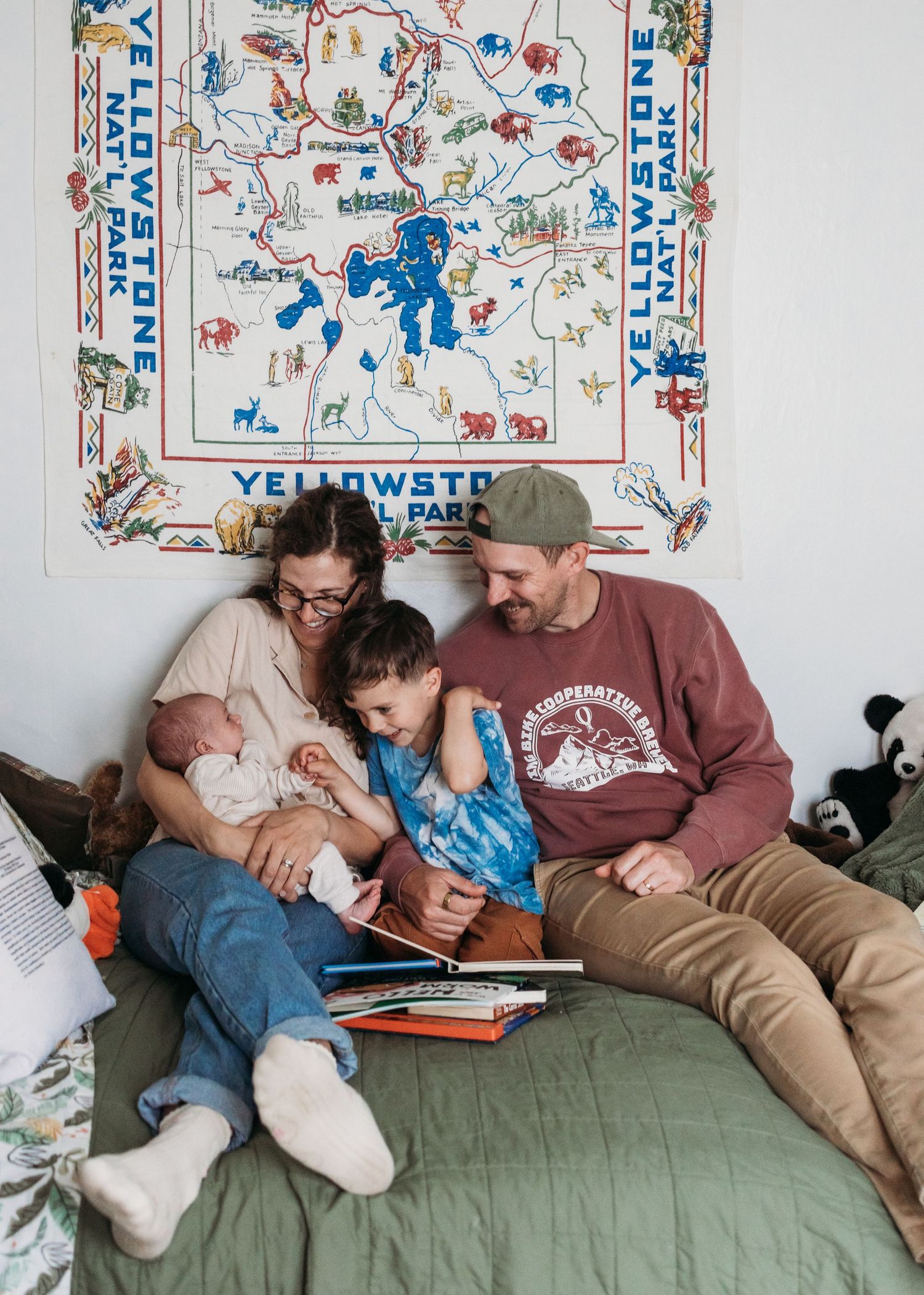 Family of four reads together on a bed beneath a Yellowstone National Park map tapestry in a cozy bedroom.