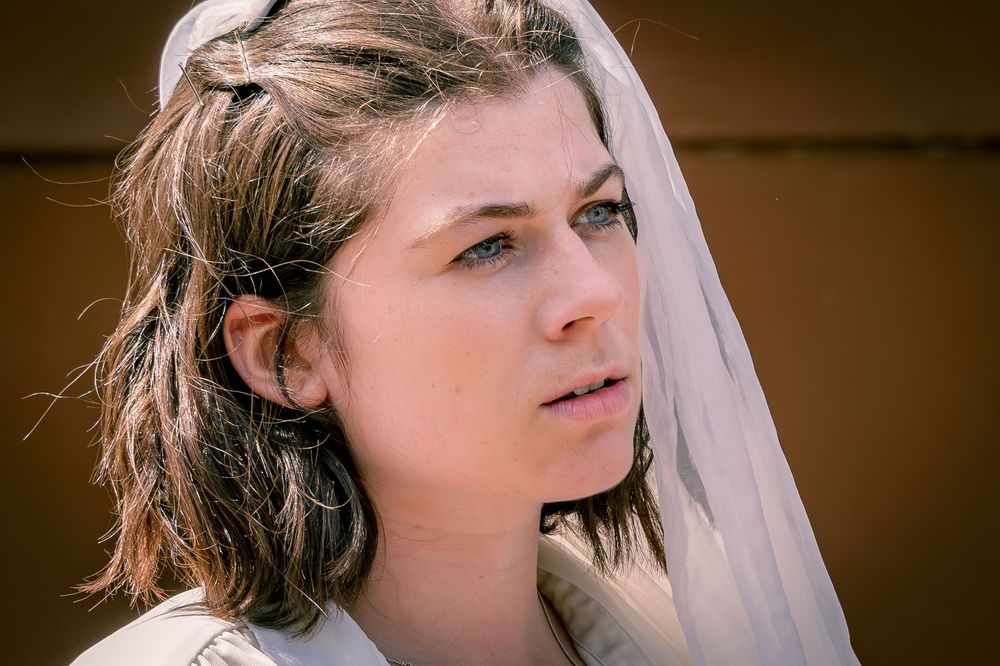 Young woman with wet hair wearing a white veil headscarf, gazing thoughtfully in natural light.