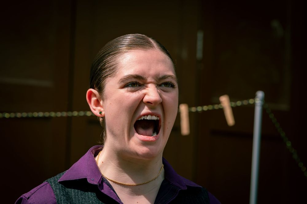 Woman in purple shirt shouting with mouth wide open, expressing intense emotion or anger.