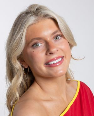 Close-up portrait of a smiling blonde woman with blue eyes wearing a red top and hoop earrings.