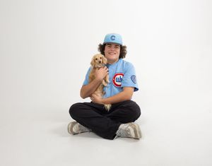Smiling young man in Chicago Cubs jersey sits cross-legged holding an adorable golden puppy on white background.