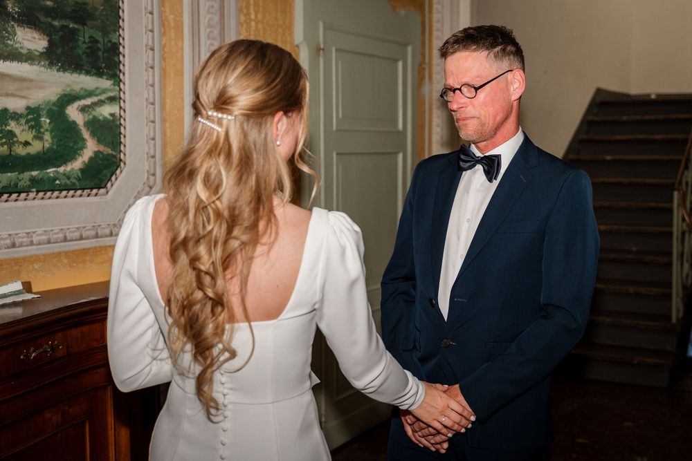 Bride and groom holding hands during an intimate wedding ceremony moment, bride in white gown with flowing curls.