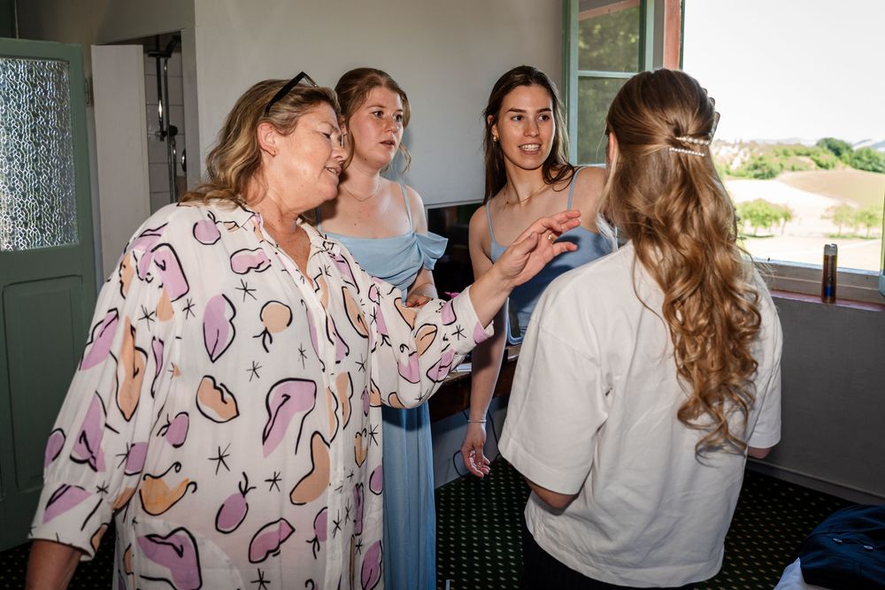 Women in bridal party getting ready together, adjusting dresses in a bright room before the wedding ceremony.