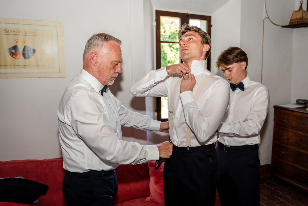 Two men helping a groom adjust his tie while getting ready for a wedding ceremony indoors.