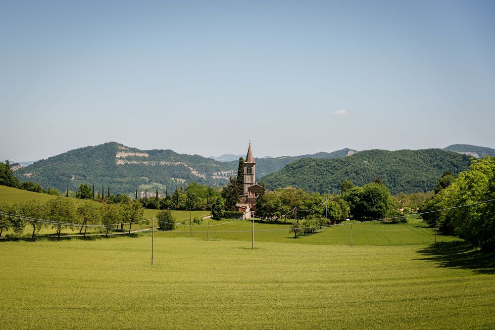 Scenic Italian countryside landscape with historic church tower surrounded by green hills and trees.